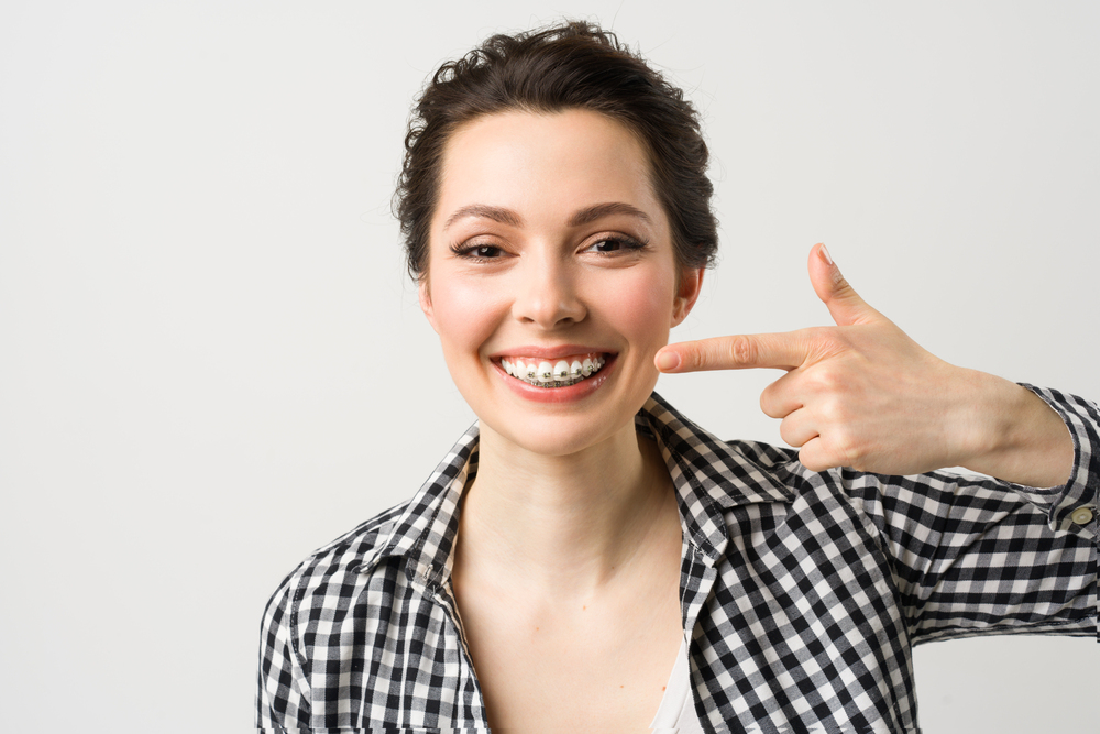 A smiling woman points to her metal braces. Orthodontic options like these may be available from dentists or orthodontists in Henderson, NV.